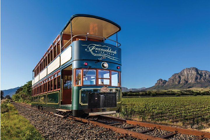 Experience the charm of Franschhoek as you ride the wine tram surrounded by stunning vineyards and dramatic mountains perfect for savoring exquisite wines and culinary delights.